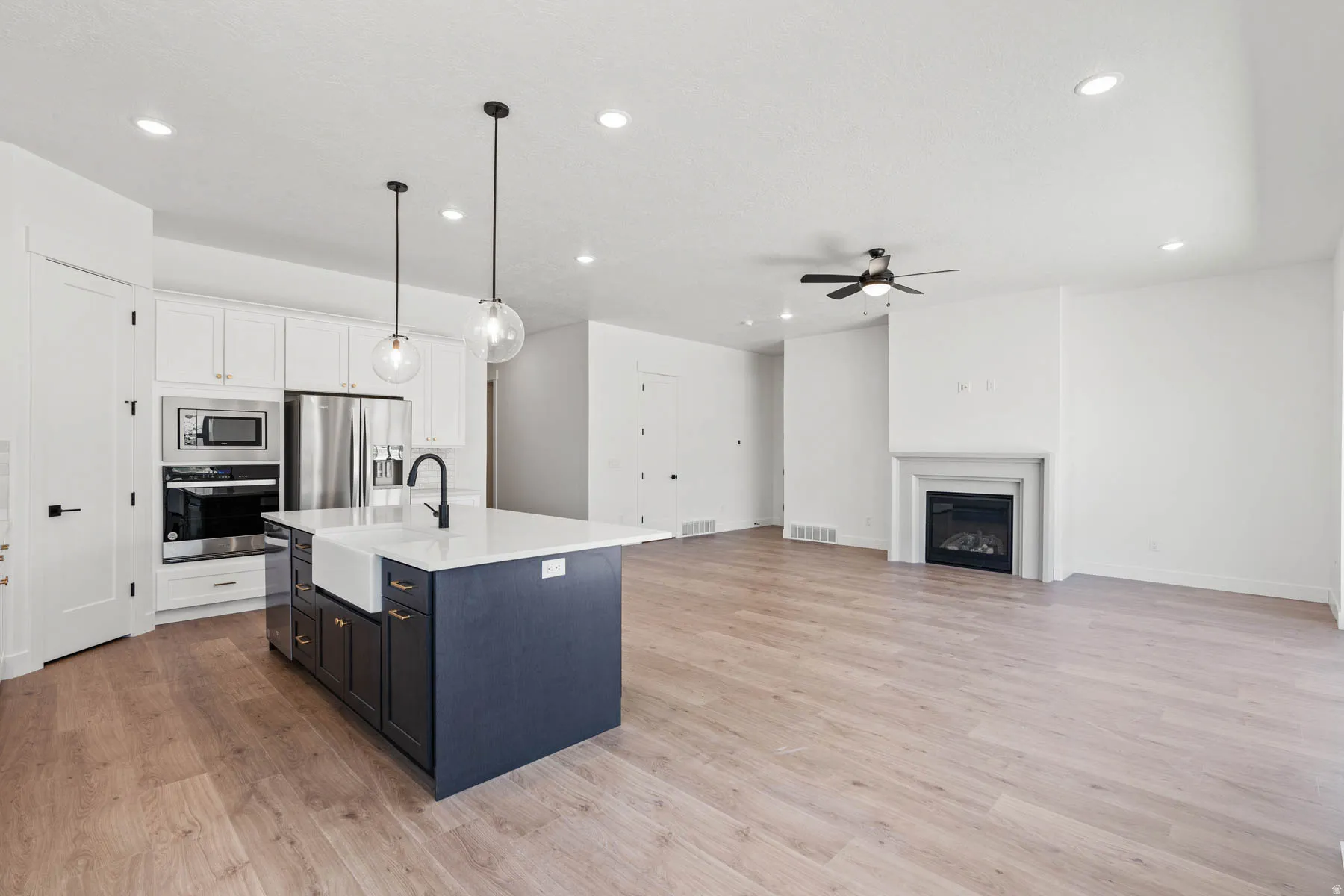 Kitchen featuring two tone cabinetry, decorative light fixtures, stainless steel appliances, open floor plan, and an island with sink