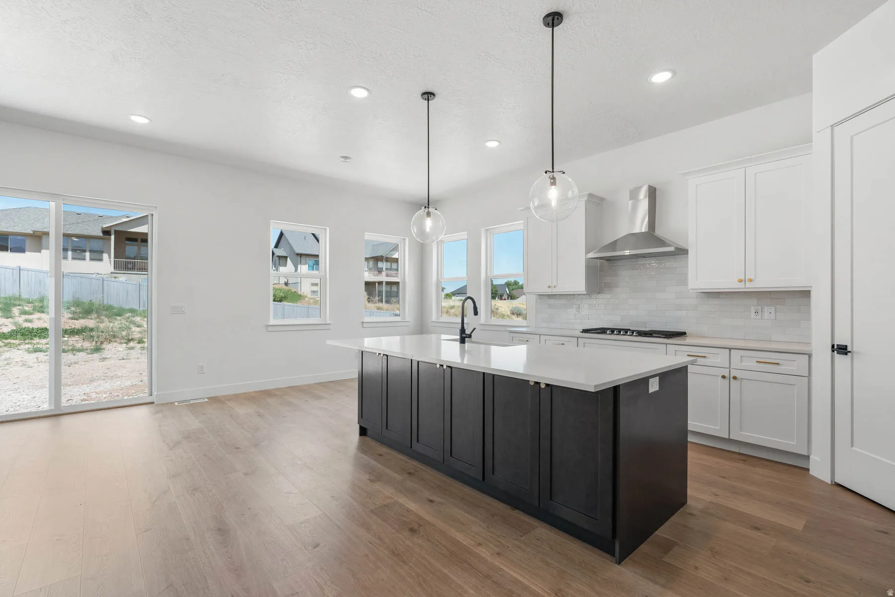 Two tone kitchen featuring two tone color scheme, a kitchen island with sink, light wood-style floors, hanging light fixtures, and light stone countertops