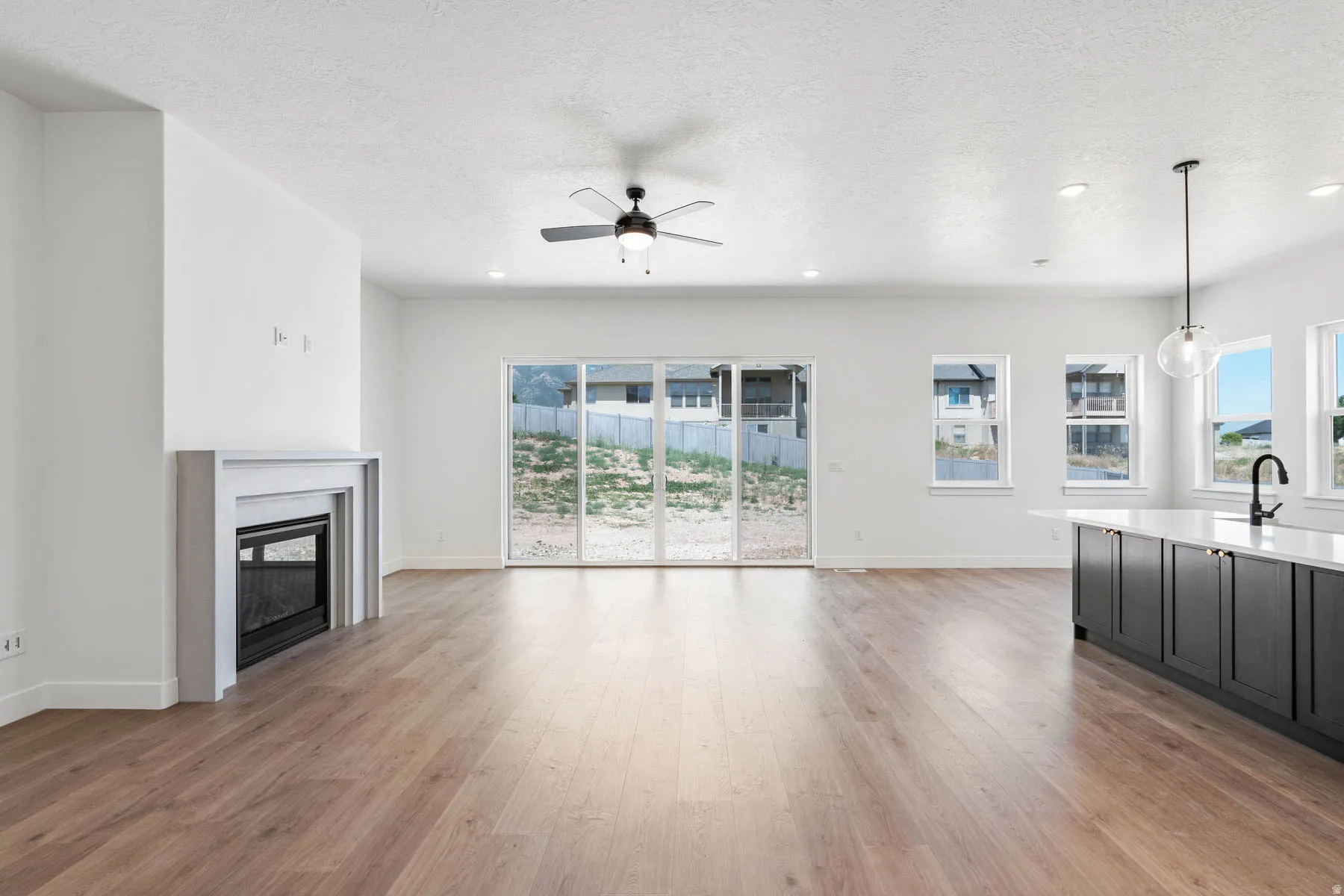 Unfurnished living room featuring light wood-style floors, ceiling fan, a fireplace, a textured ceiling, and recessed lighting