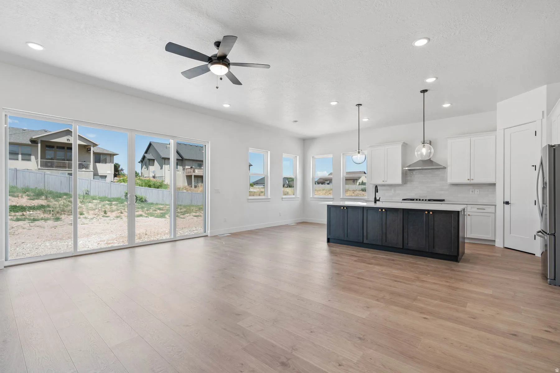 Two tone kitchen featuring open floor plan, light countertops, an island with sink, decorative light fixtures, and freestanding refrigerator