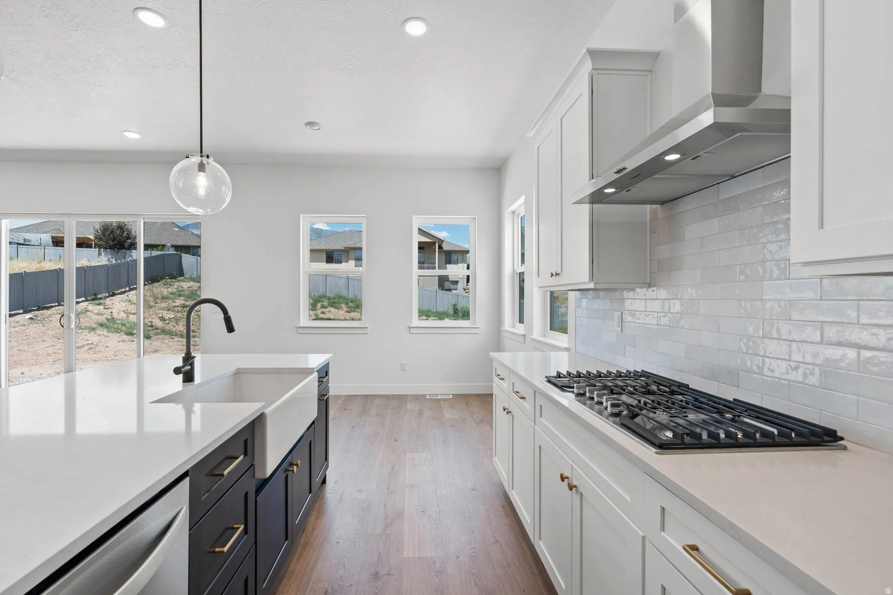 Two tone kitchen with dual tone cabinetry, light stone counters, dark wood-style flooring, pendant lighting, and stainless steel appliances