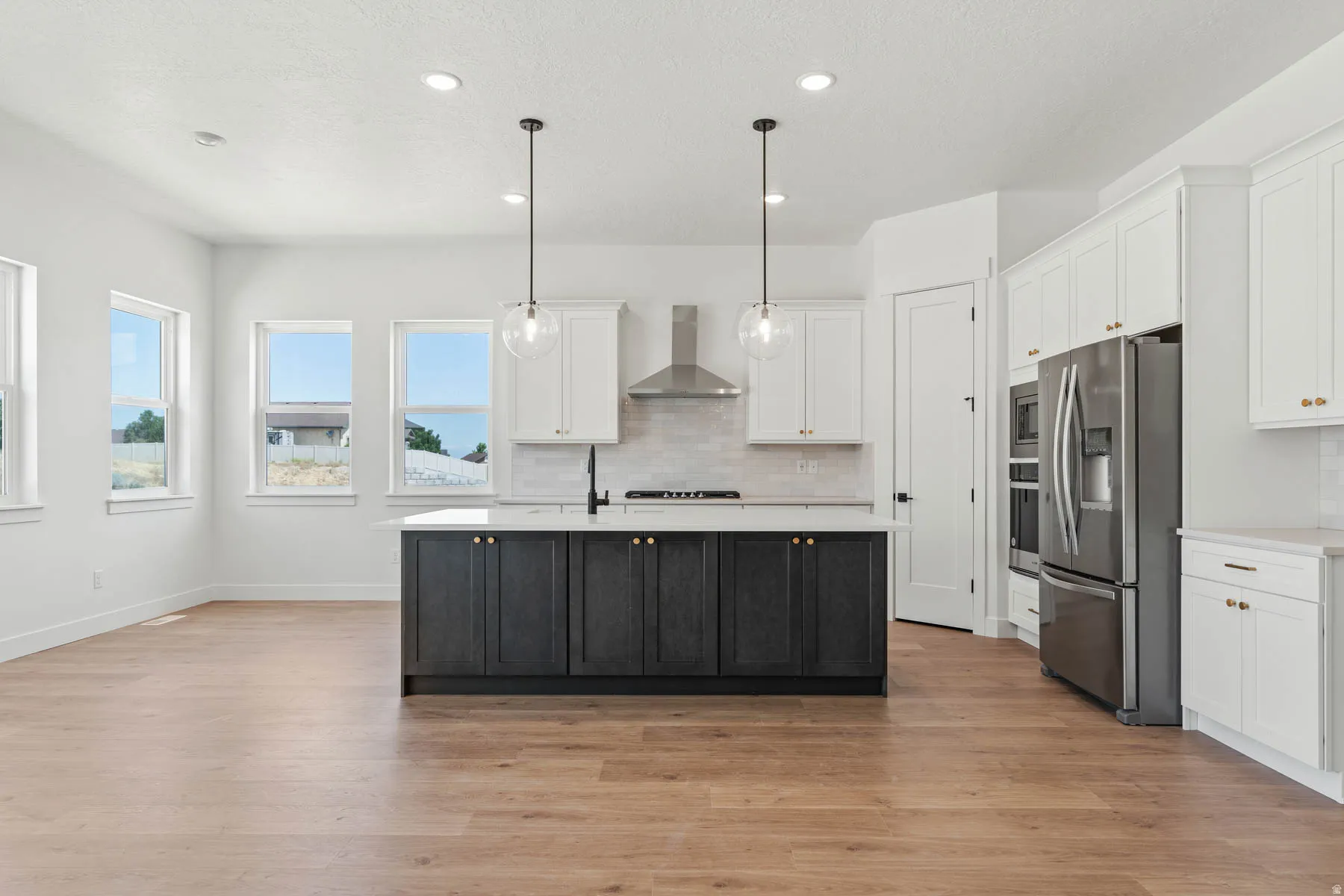 Dual tone kitchen featuring stainless steel appliances, pendant lighting, an island with sink, light wood finished floors, and two tone color scheme