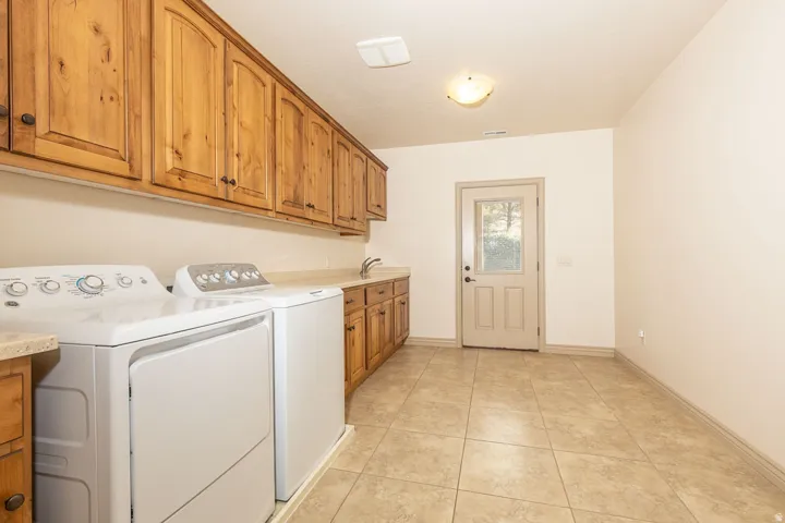Laundry room with washing machine and clothes dryer, light tile patterned floors, and cabinet space