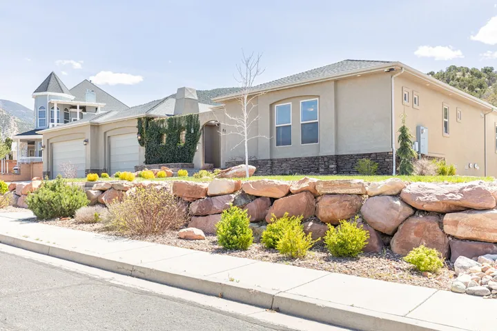 View of front of home with stucco siding, an attached garage, stone siding, and a chimney