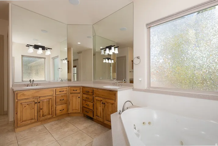 Full bathroom featuring double vanity, light tile patterned flooring, and a whirlpool tub