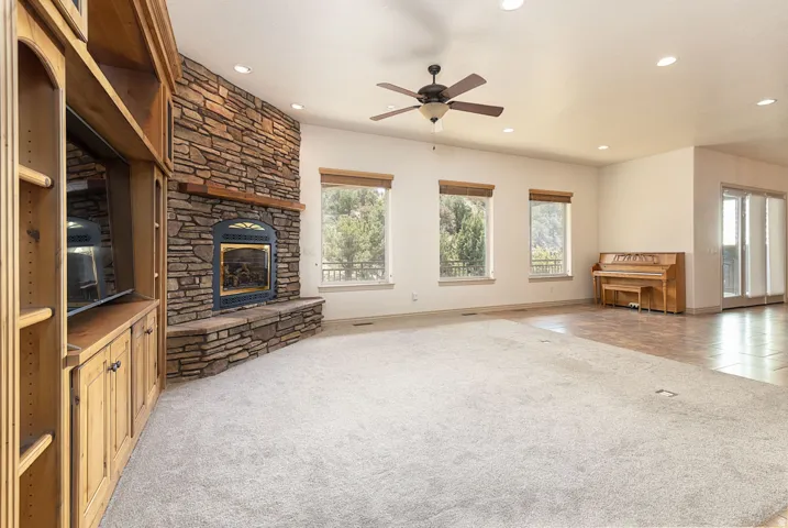 Unfurnished living room with light carpet, a stone fireplace, ceiling fan, and recessed lighting