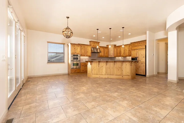 Kitchen featuring a kitchen island with sink, paneled built in fridge, stainless steel double oven, dark countertops, and wood finish cabinets