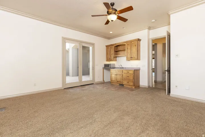 Kitchen featuring ceiling fan, crown molding, open shelves, light colored carpet, and stainless steel microwave