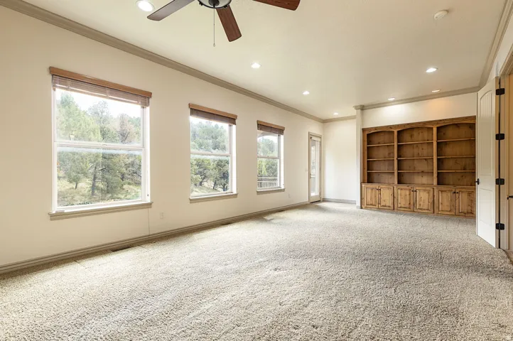 Unfurnished living room featuring ceiling fan, recessed lighting, light carpet, crown molding, and built in features