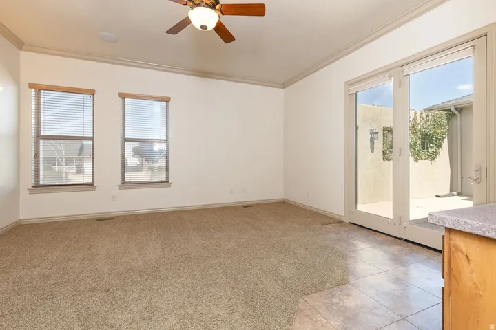 Empty room featuring a ceiling fan, crown molding, light tile patterned floors, and light carpet