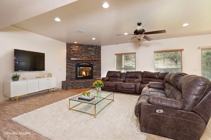 Carpeted living area with ceiling fan, a stone fireplace, and recessed lighting
