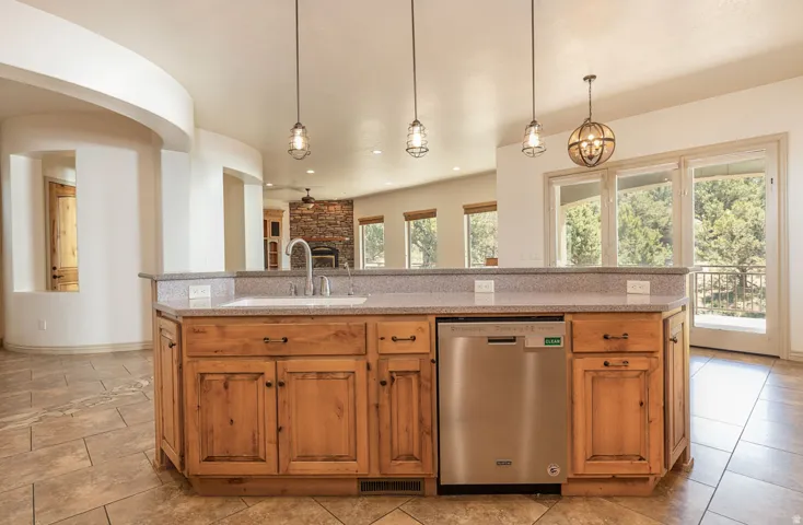 Kitchen featuring stainless steel dishwasher, light stone countertops, and decorative light fixtures