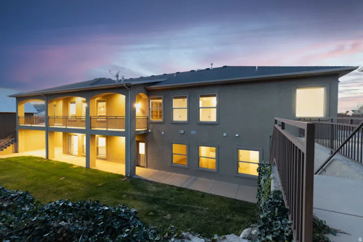 Back of property at dusk featuring a patio, a lawn, stucco siding, and a balcony