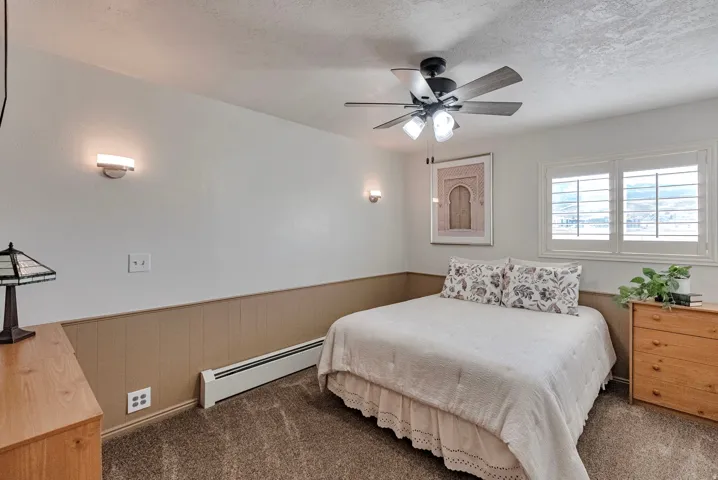 Bedroom with a wainscoted wall, a baseboard radiator, dark carpet, a textured ceiling, and a ceiling fan