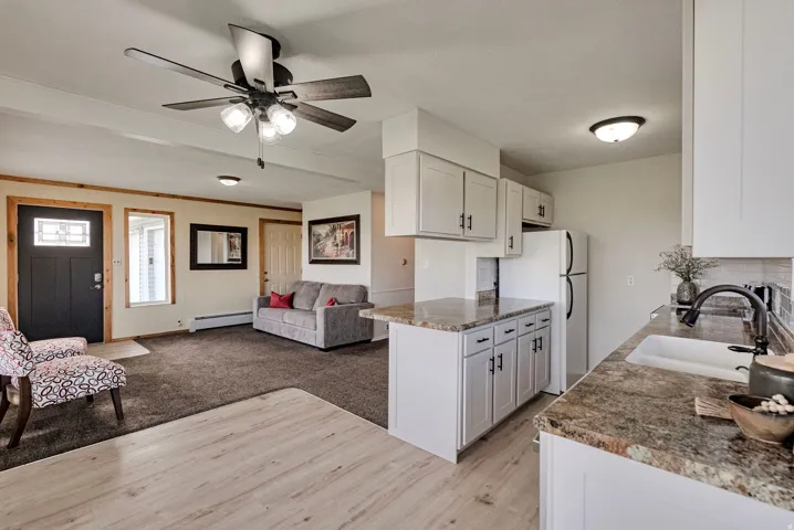 Kitchen with white cabinets, freestanding refrigerator, ceiling fan, open floor plan, and baseboard heating