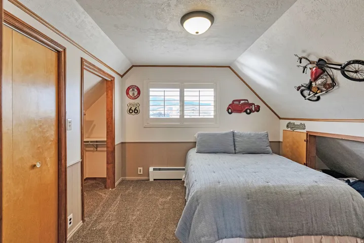 Bedroom with a closet, wainscoting, dark colored carpet, and a baseboard heating unit. Notice the open cubby - perfect for a child's single bed.