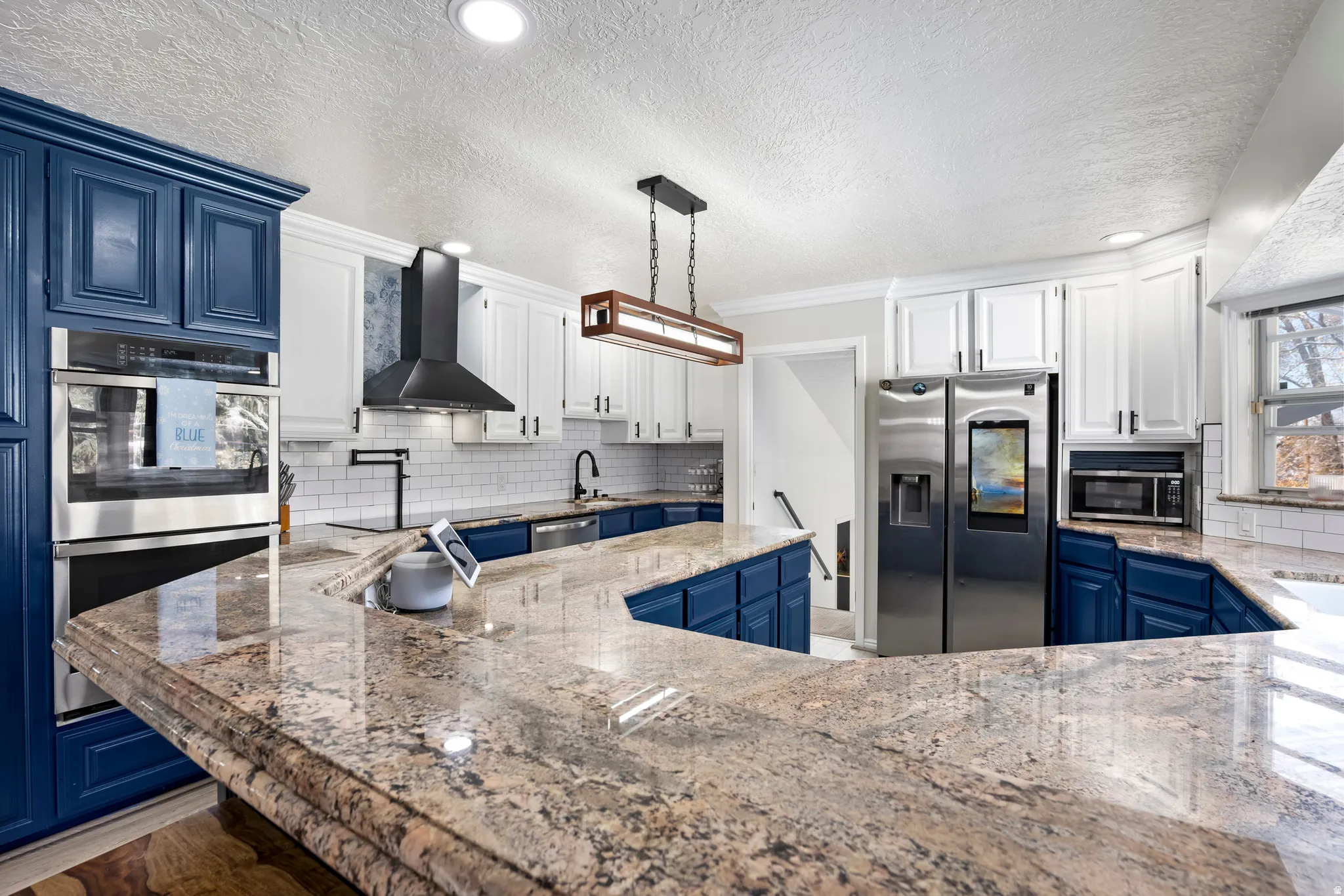Kitchen featuring stainless steel appliances, dual tone cabinetry, light stone counters, hanging light fixtures, and crown molding