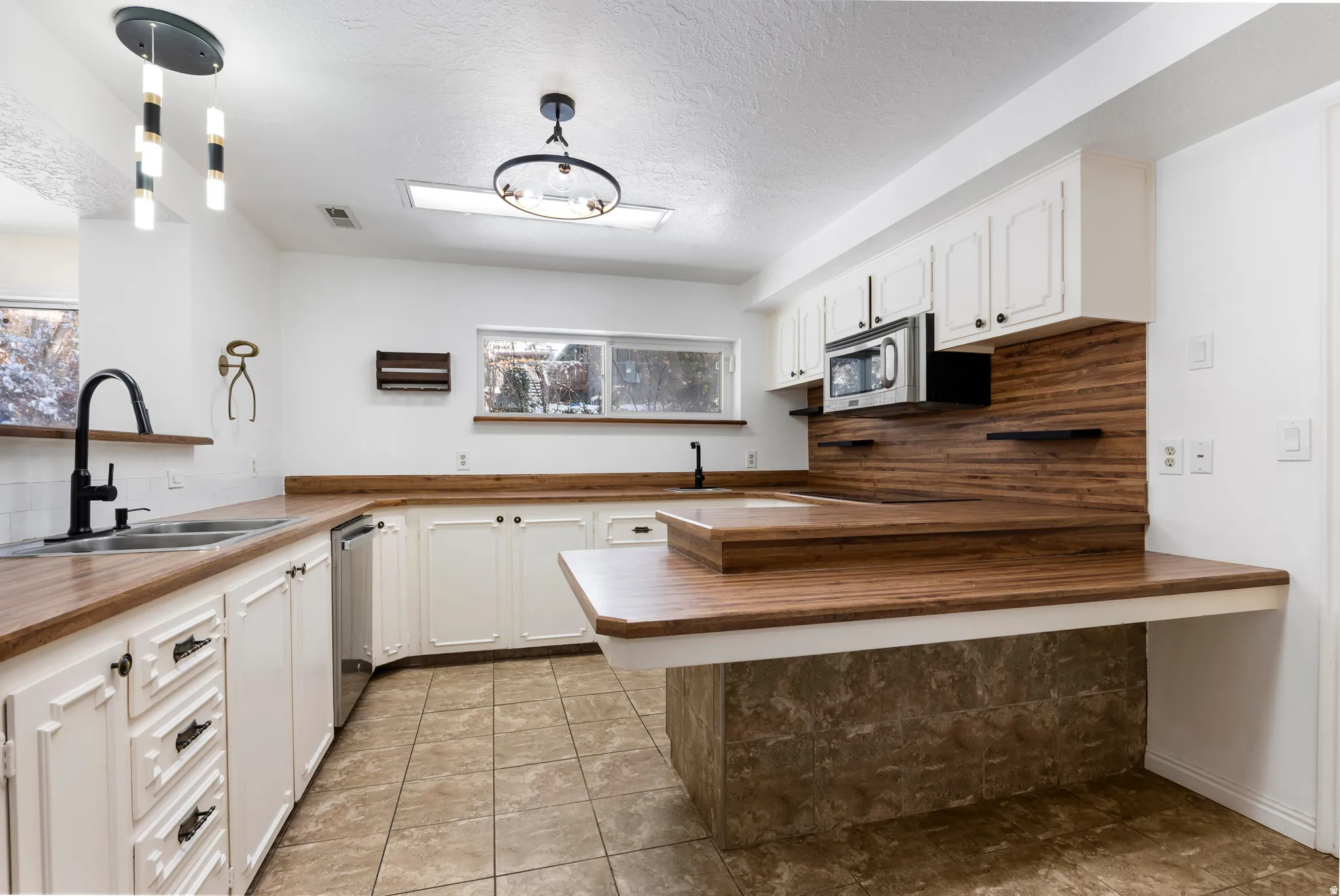 Kitchen featuring a peninsula, white cabinets, wooden counters, a textured ceiling, and stainless steel appliances