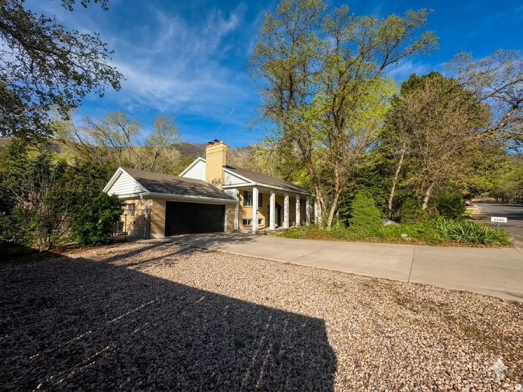 View of home's exterior featuring a garage, concrete driveway, a porch, a chimney, and brick siding