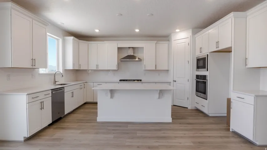 Kitchen featuring white cabinets, a kitchen island, light wood-style floors, stainless steel appliances, and recessed lighting