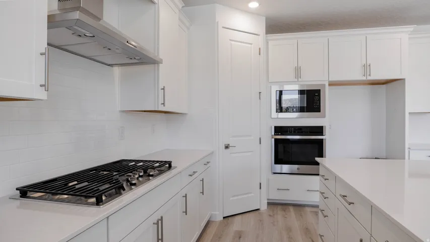Kitchen featuring white cabinets, stainless steel appliances, light wood-style flooring, and light stone countertops