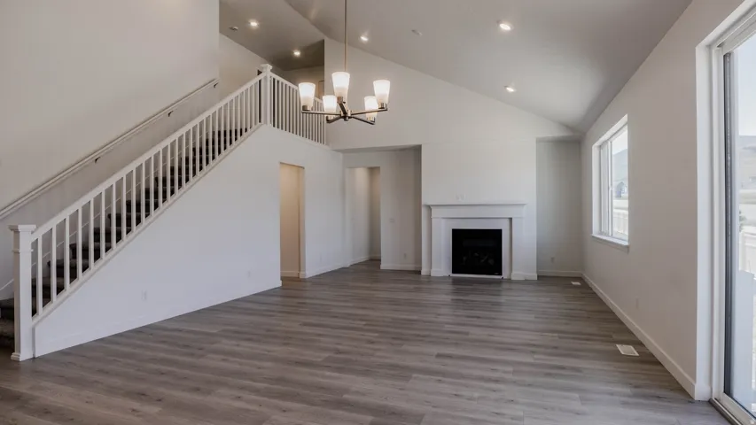 Unfurnished living room with hanging lights, vaulted ceiling, dark wood finished floors, and a fireplace