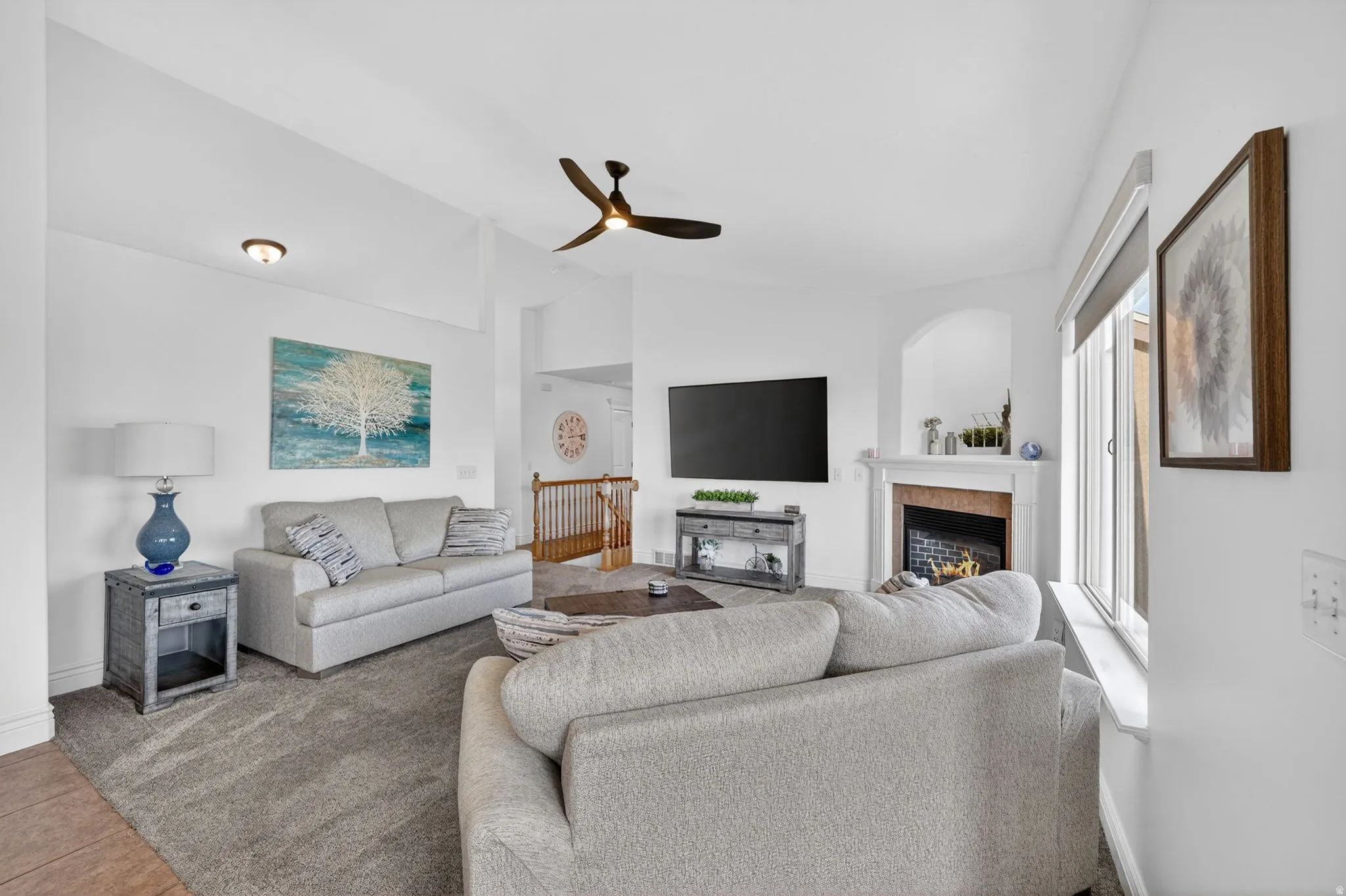 Living room featuring lofted ceiling, a ceiling fan, and a tiled fireplace