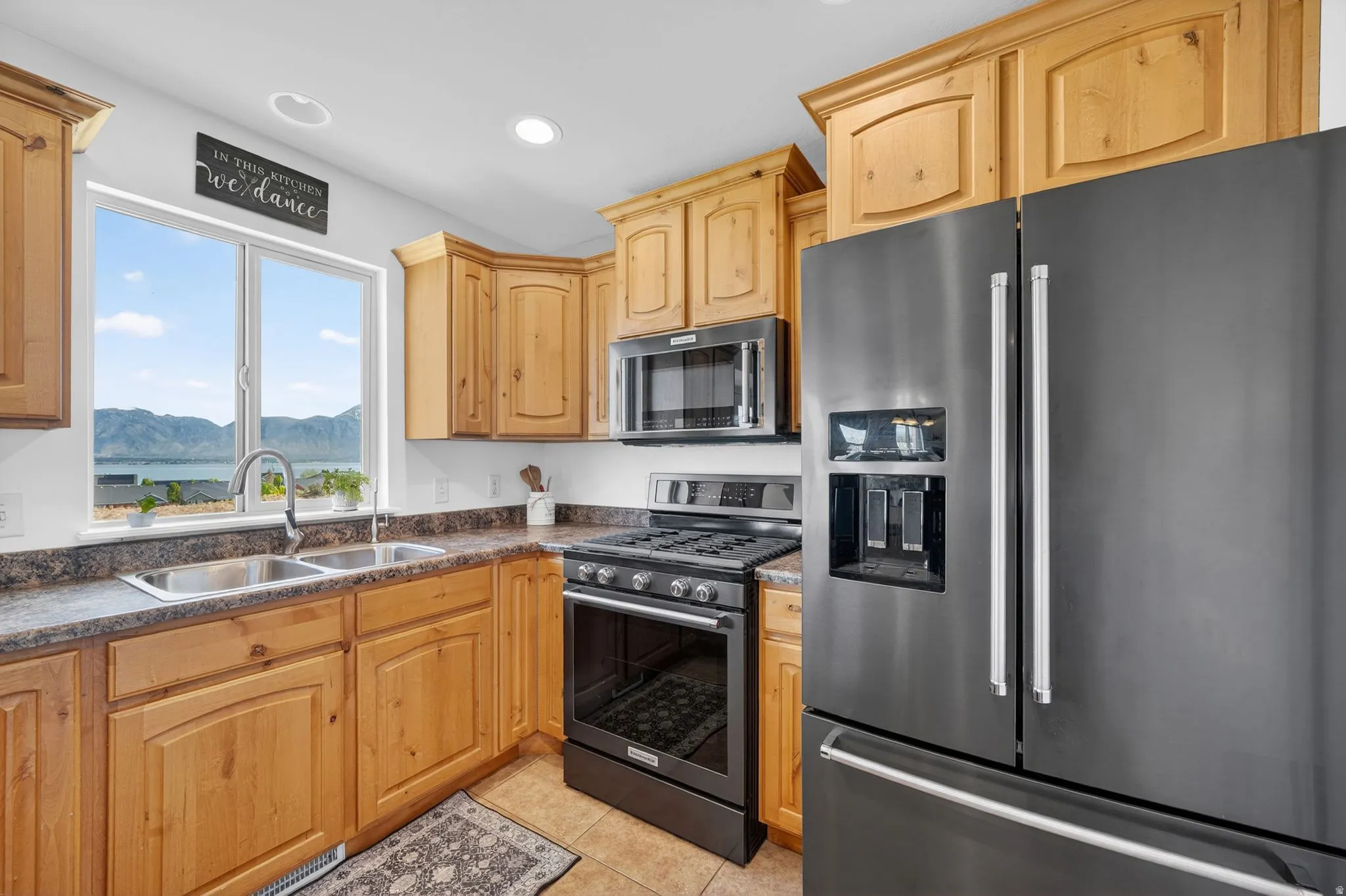 Kitchen with stainless steel refrigerator with ice dispenser, gas stove, a mountain view, light tile patterned flooring, and recessed lighting