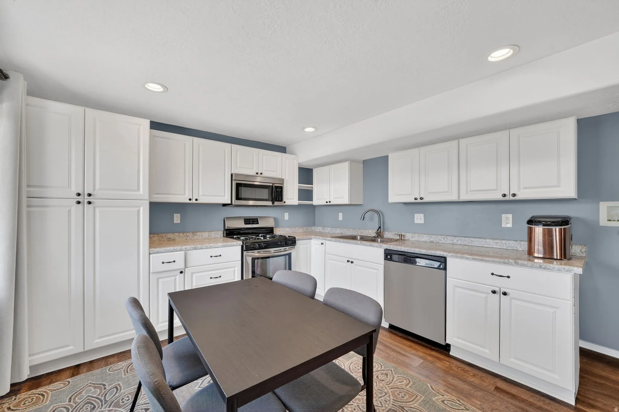 Kitchen featuring stainless steel appliances, white cabinetry, dark wood-style floors, recessed lighting, and light stone counters