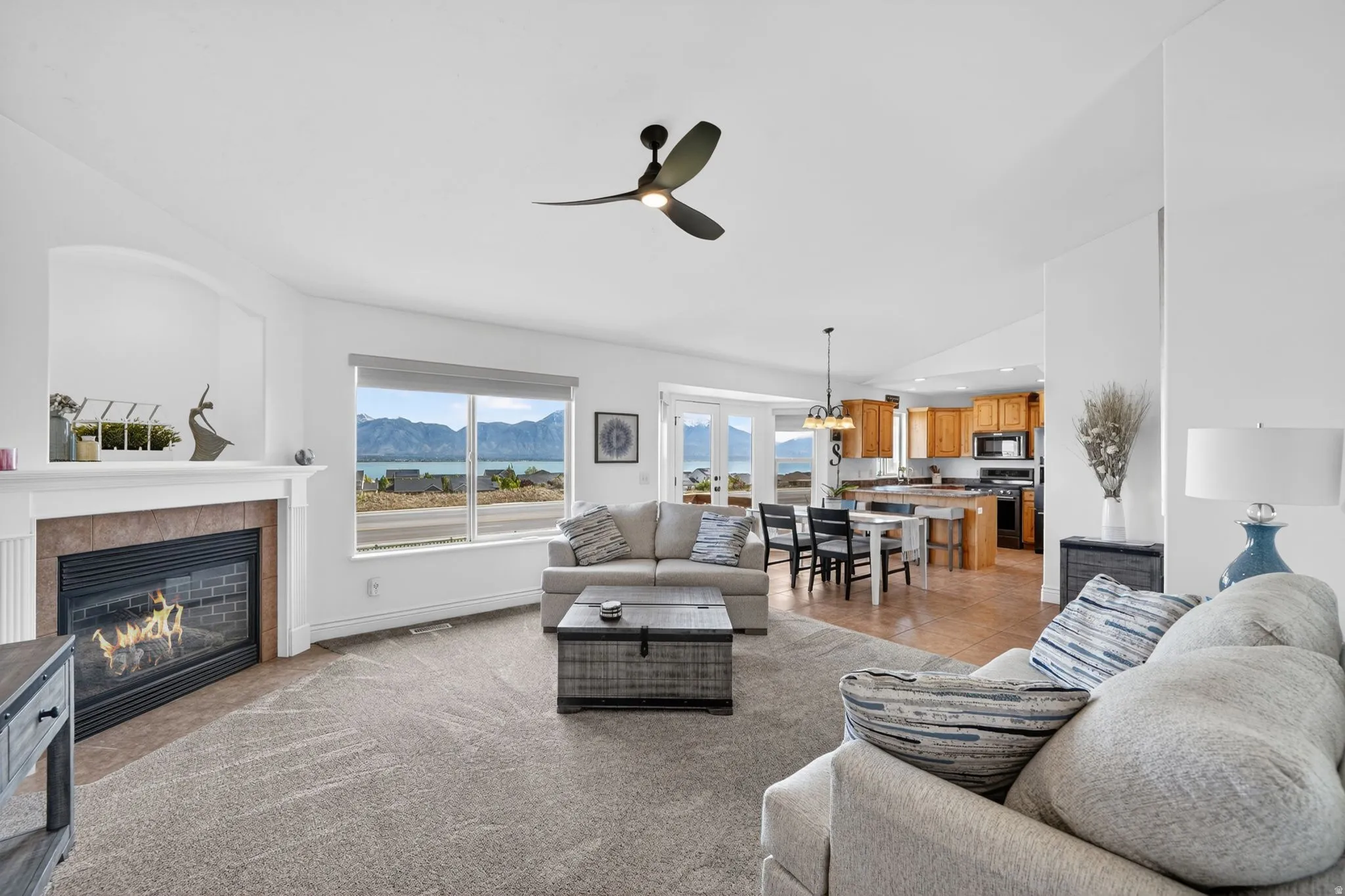 Living area with a mountain view, a ceiling fan, a fireplace, light carpet, and vaulted ceiling