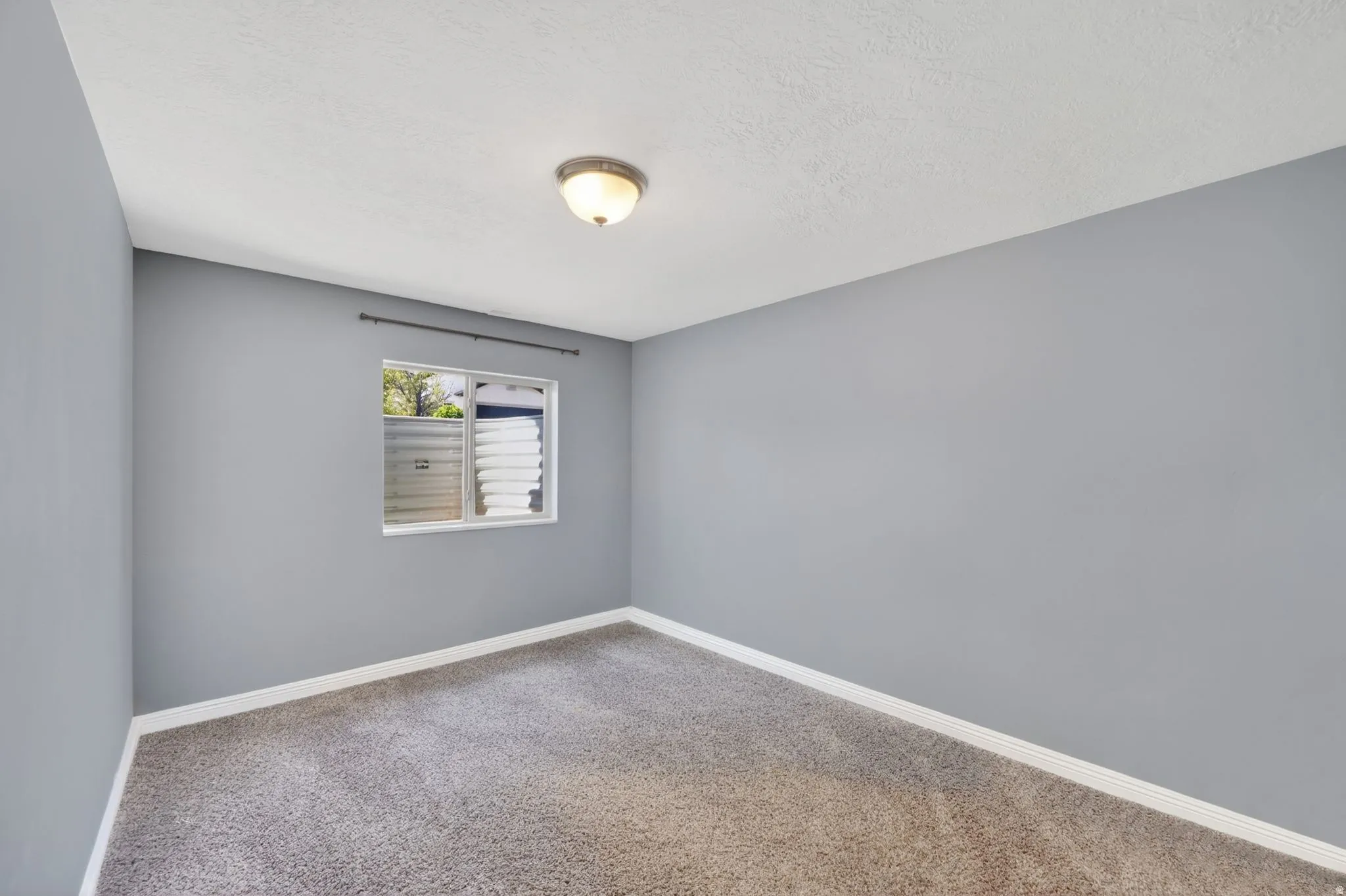 Empty room with light carpet and a textured ceiling