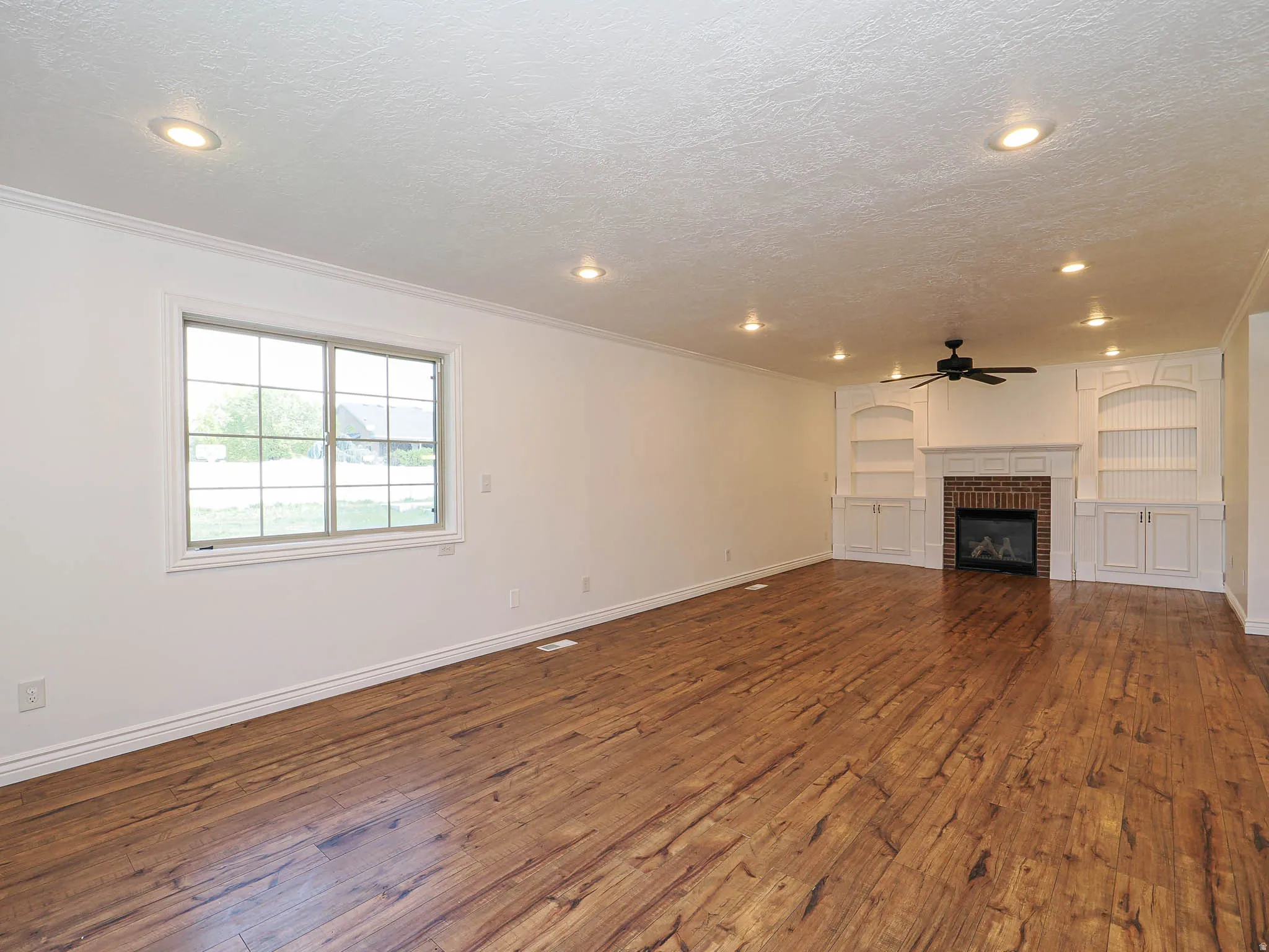 Unfurnished living room featuring a brick fireplace, built in features, dark wood finished floors, a textured ceiling, and ceiling fan