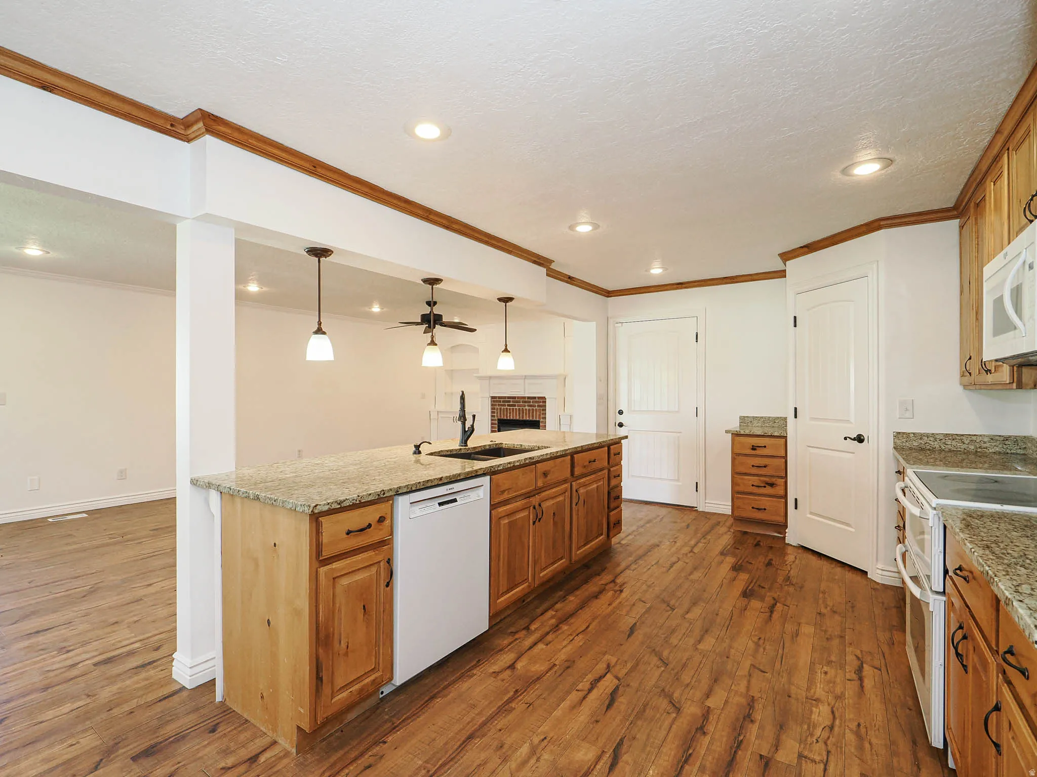 Kitchen with dark wood-type flooring, wood finish cabinets, white appliances, and crown molding