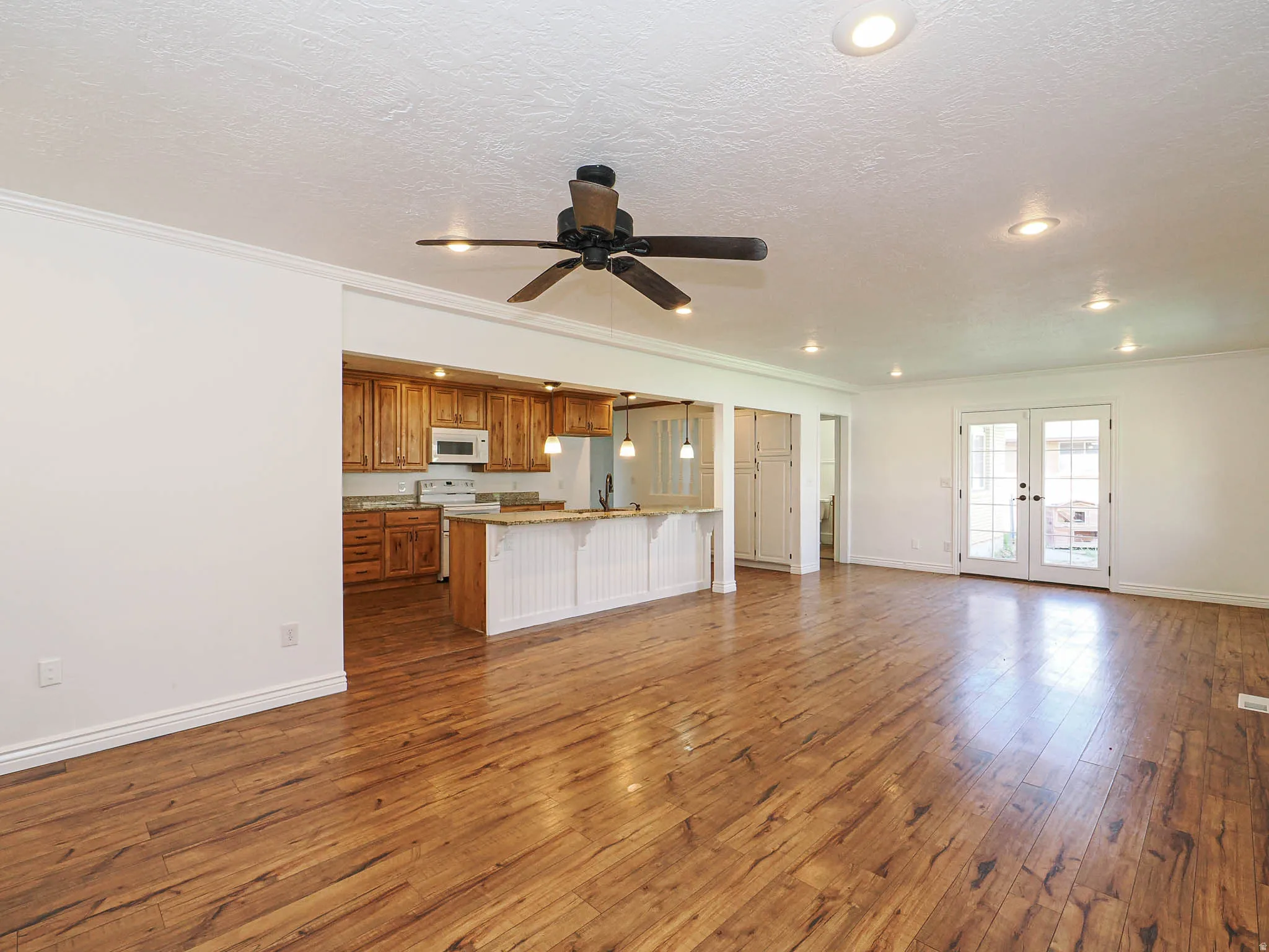 Unfurnished living room featuring dark wood-style flooring, french doors, ceiling fan, a textured ceiling, and crown molding