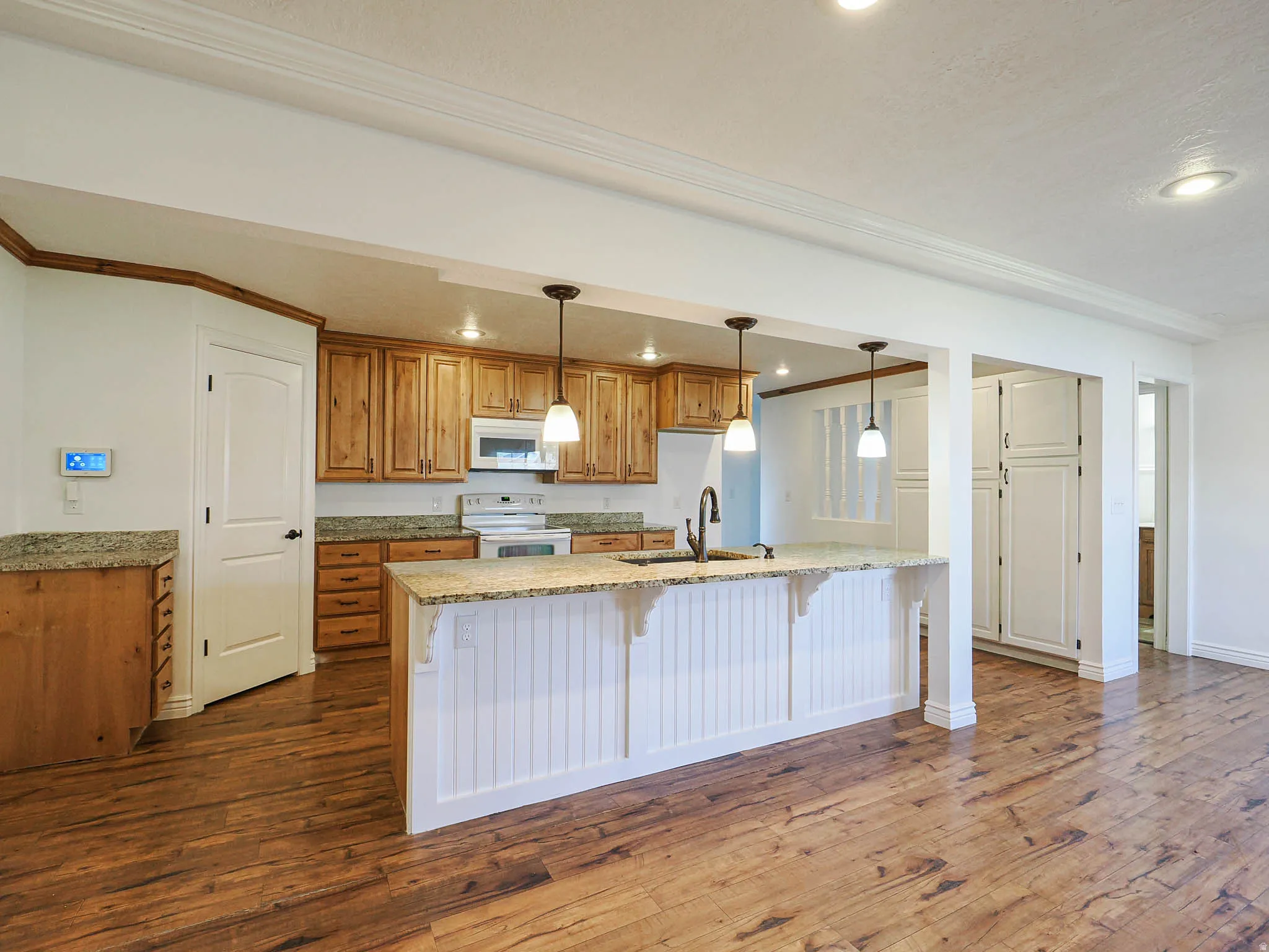 Kitchen featuring wood finish cabinetry, light stone countertops, a breakfast bar area, ornamental molding, and white appliances