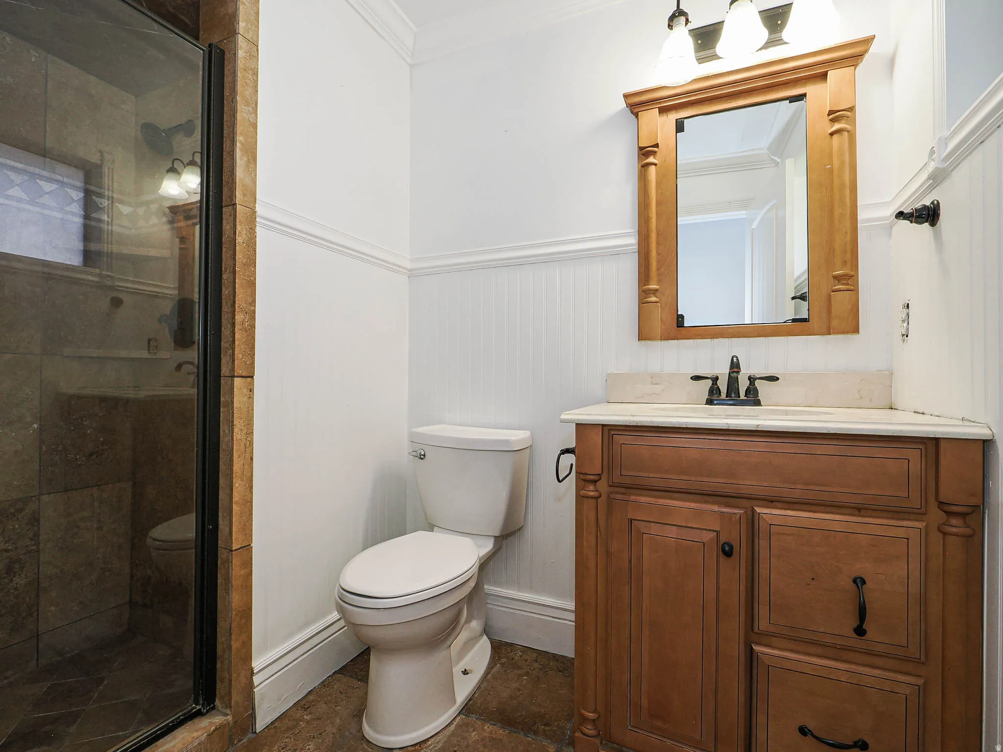 Full bathroom with vanity, a shower stall, wainscoting, and crown molding