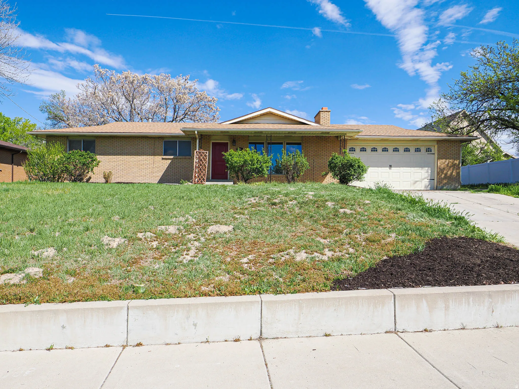 Ranch-style home featuring an attached garage, brick siding, a chimney, covered porch, and driveway