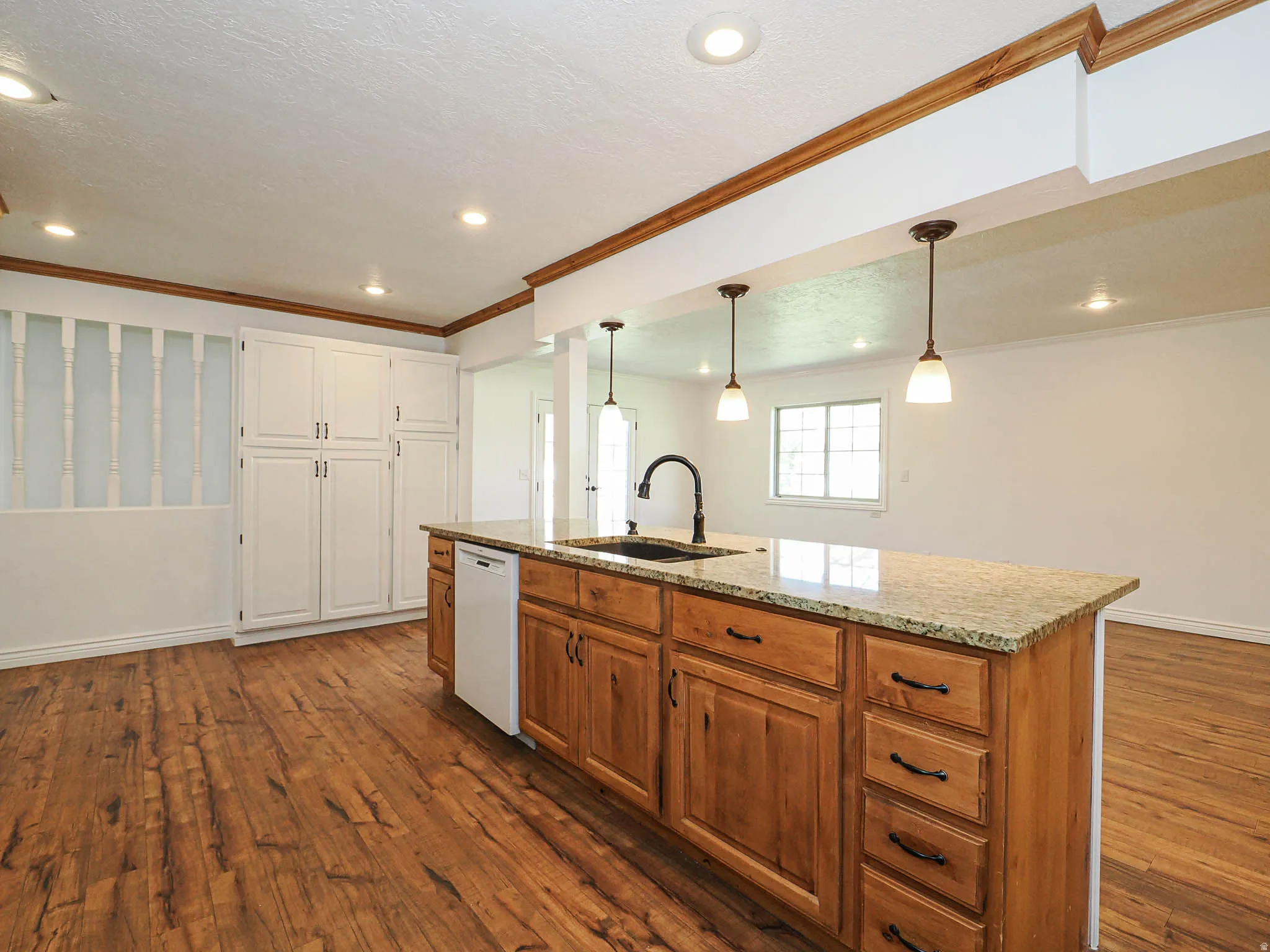 Kitchen with a center island with sink, pendant lighting, dark wood-style floors, light stone countertops, and dual tone cabinets