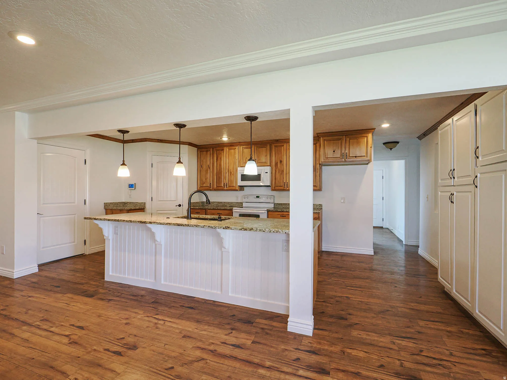 Kitchen featuring a breakfast bar area, light stone counters, dark wood finished floors, white appliances, and wood finish cabinetry