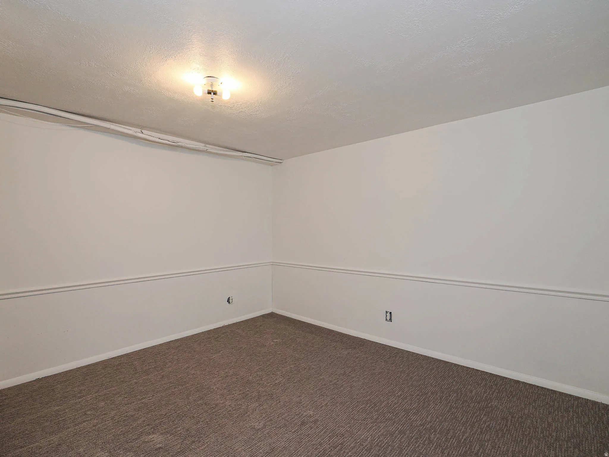Empty room featuring dark carpet and a textured ceiling