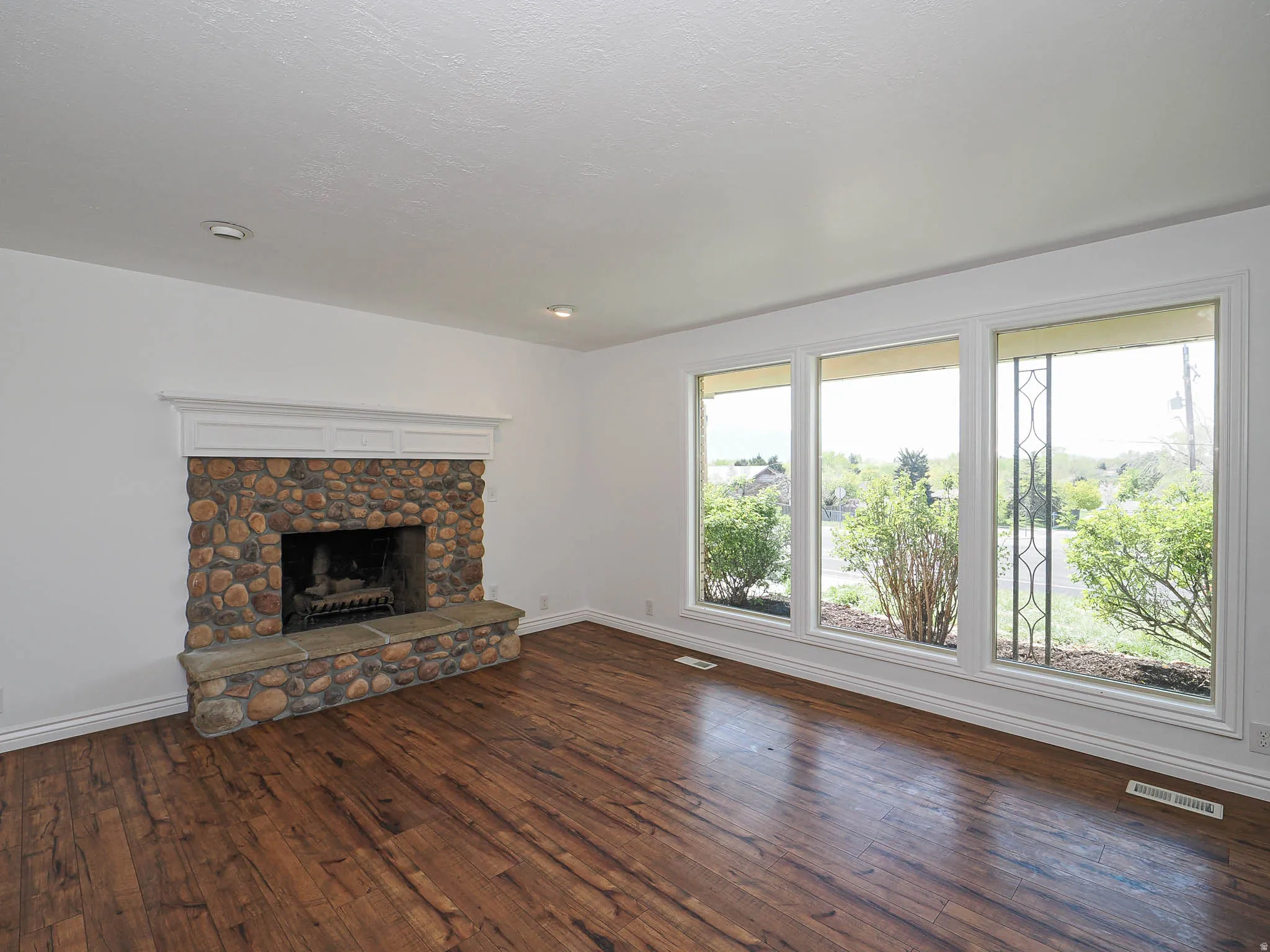 Unfurnished living room featuring a stone fireplace and dark wood-style flooring