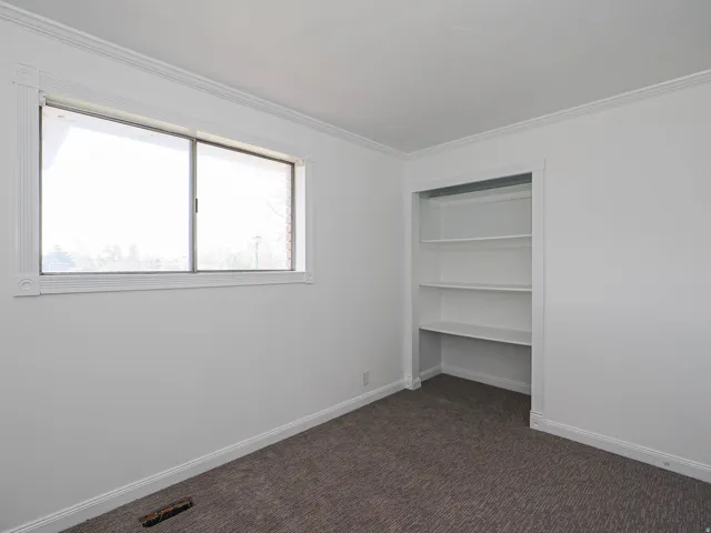 Unfurnished bedroom with dark carpet, crown molding, and a closet