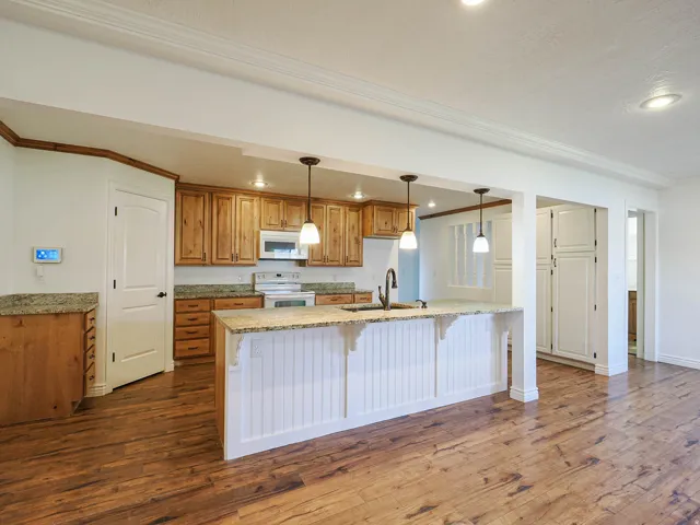 Kitchen featuring wood finish cabinetry, light stone countertops, a breakfast bar area, ornamental molding, and white appliances