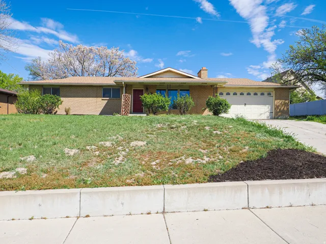 Ranch-style home featuring an attached garage, brick siding, a chimney, covered porch, and driveway