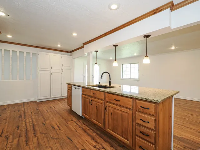 Kitchen with a center island with sink, pendant lighting, dark wood-style floors, light stone countertops, and dual tone cabinets