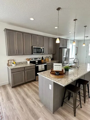 Kitchen featuring stainless steel appliances, a breakfast bar, light wood-style floors, pendant lighting, and dark wood finish cabinetsPhotos of Dixon Model Home for reference only. Finishes may vary from photos shown.