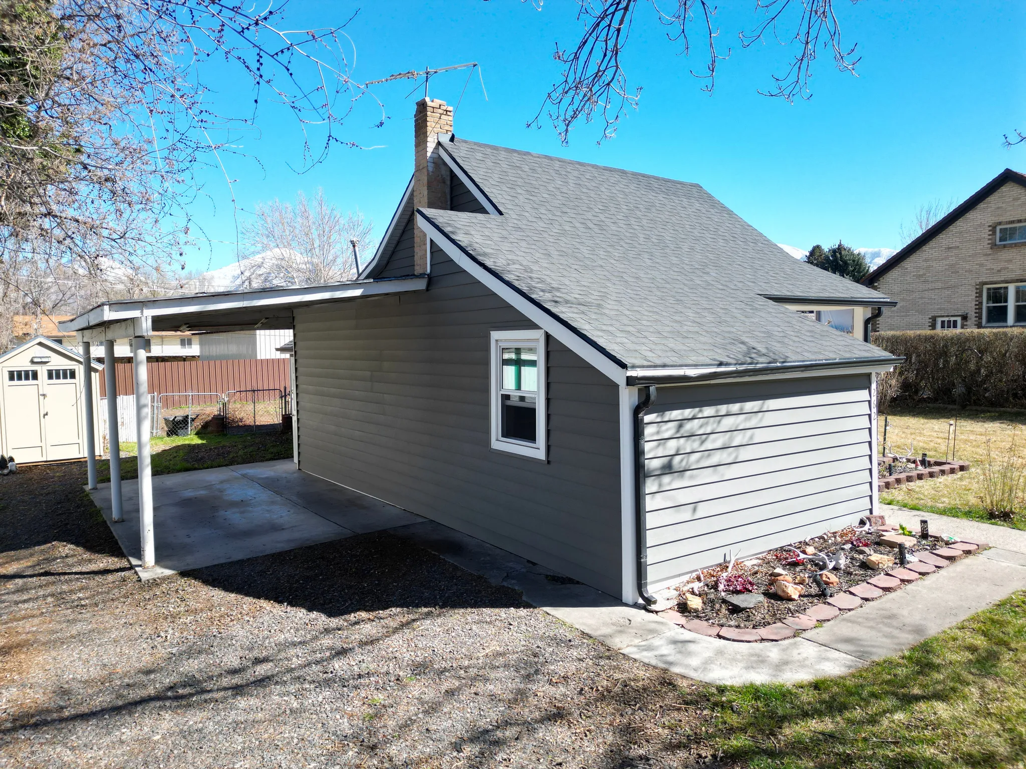 View of side of property with a chimney, a storage unit, a shingled roof, and an attached carport