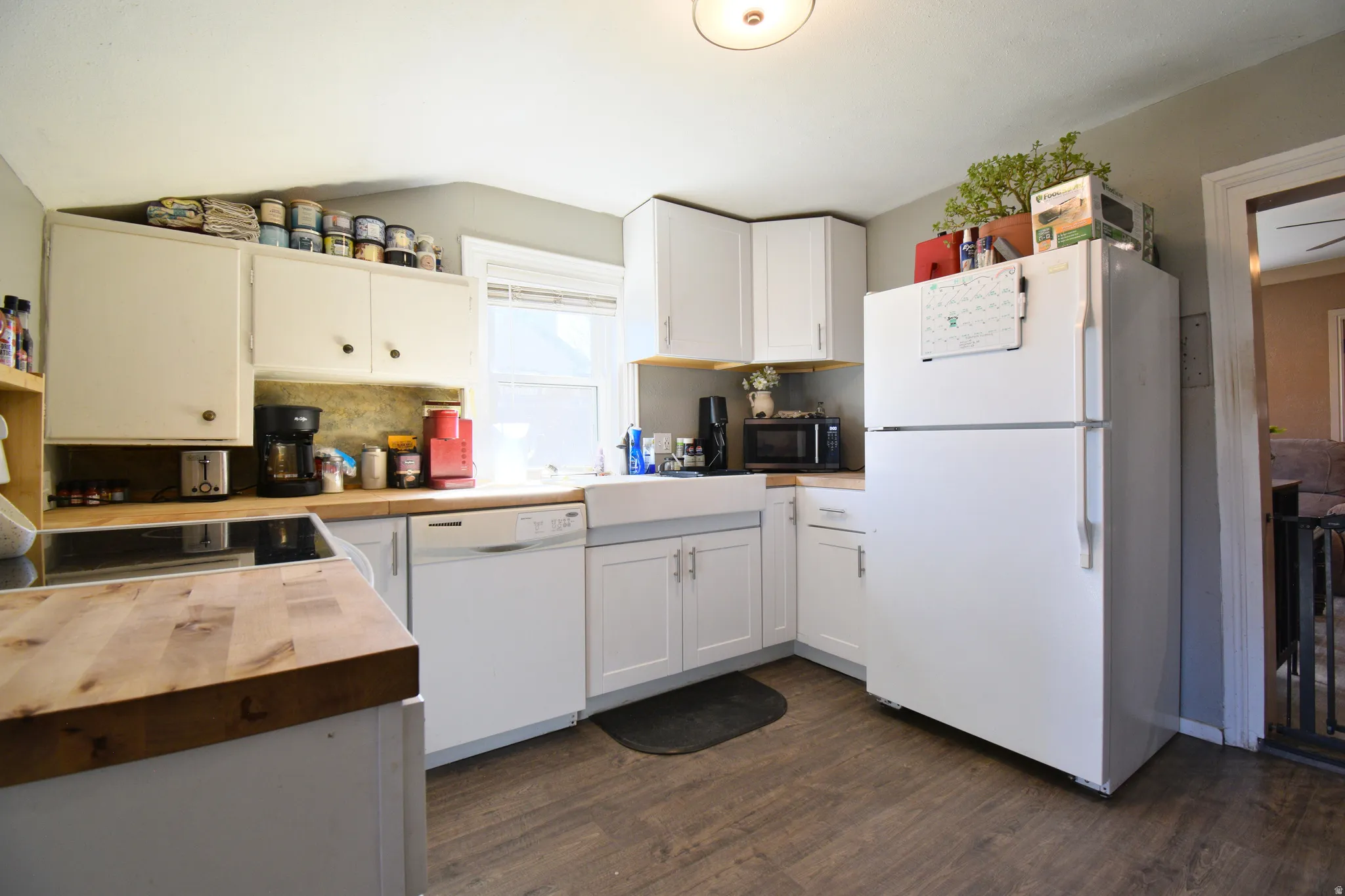 Kitchen with white appliances, white cabinetry, butcher block counters, tasteful backsplash, and dark wood-type flooring