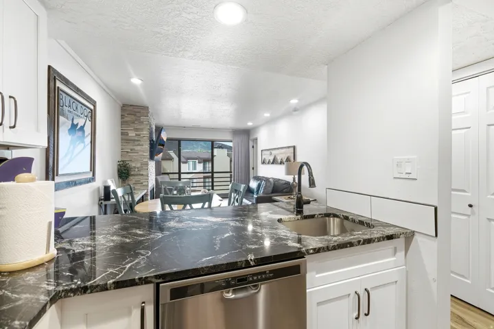 Kitchen featuring a textured ceiling, white cabinets, open floor plan, stainless steel dishwasher, and dark stone counters