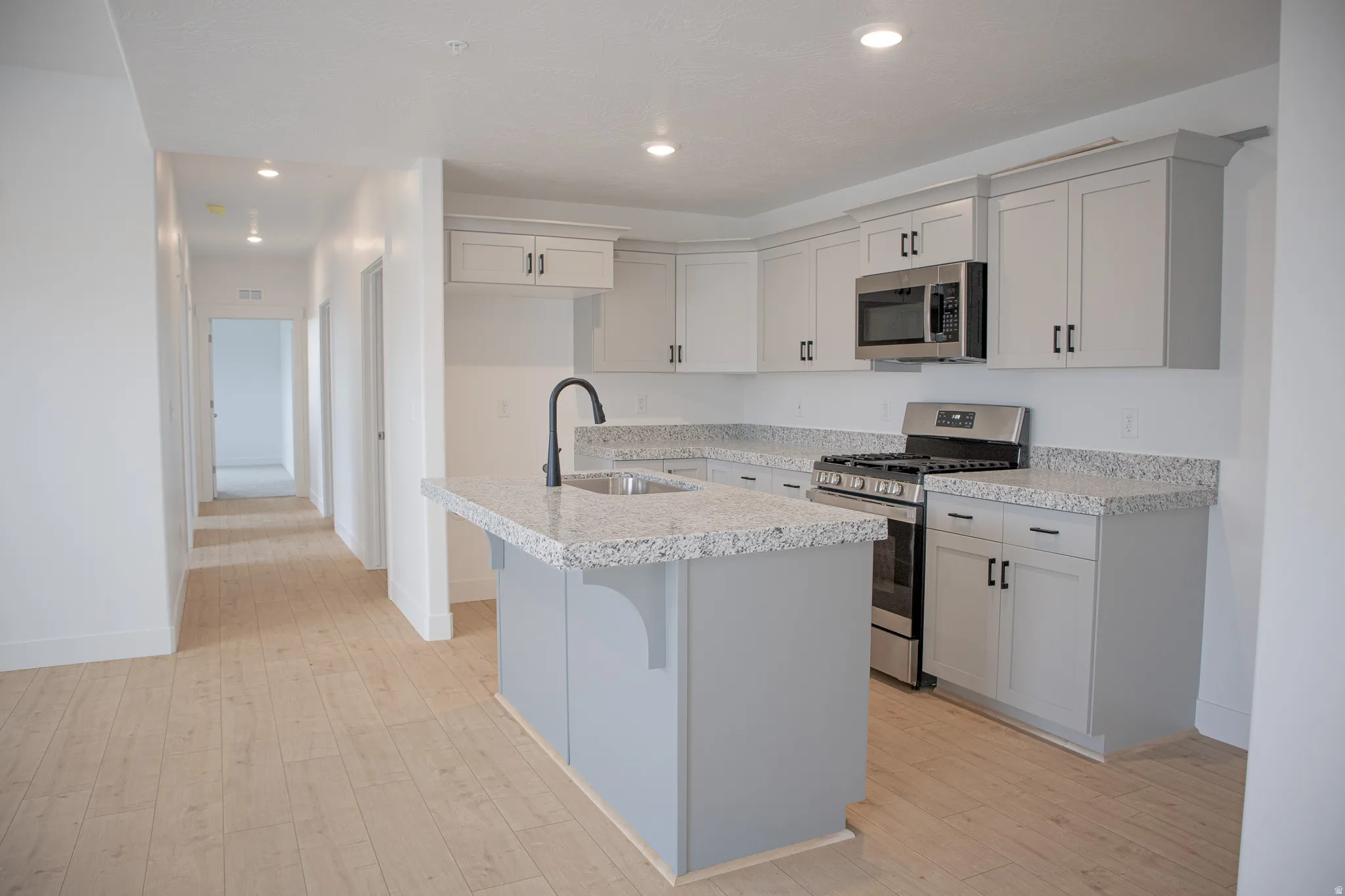 Kitchen with painted wood cabinets, granite slab countertops, gas range, microwave, dishwasher and disposal.